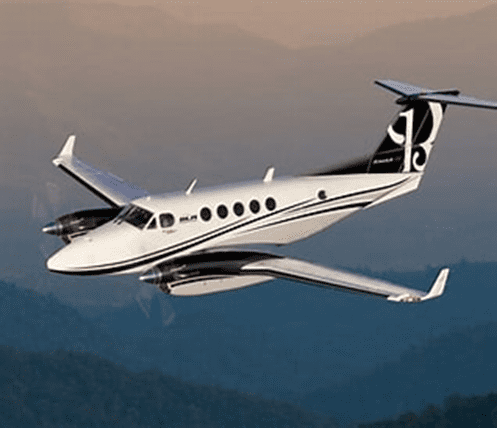 A sleek twin-engine aircraft soaring above mountain ranges during sunset, showcasing its elegant black and white design and modern aesthetics.