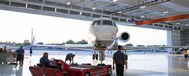 Business jet being serviced in a hangar, with technicians working on maintenance. The spacious interior showcases modern aviation facilities.