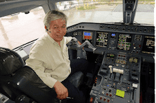 Pilot in cockpit, smiling and seated at controls with various instruments and screens visible. Highlights the aviation environment and pilot experience.
